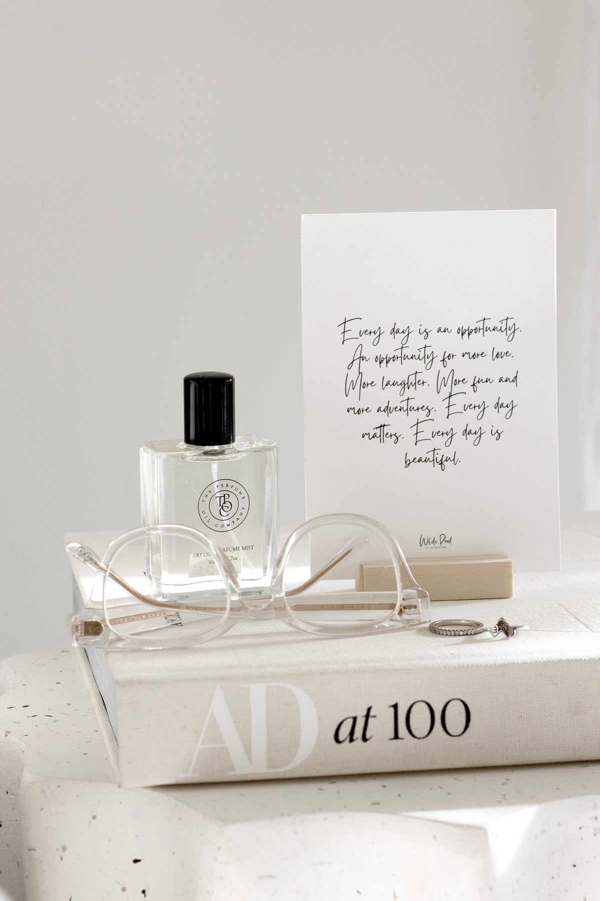 Affirmation card on a wooden stand beside a perfume bottle and book