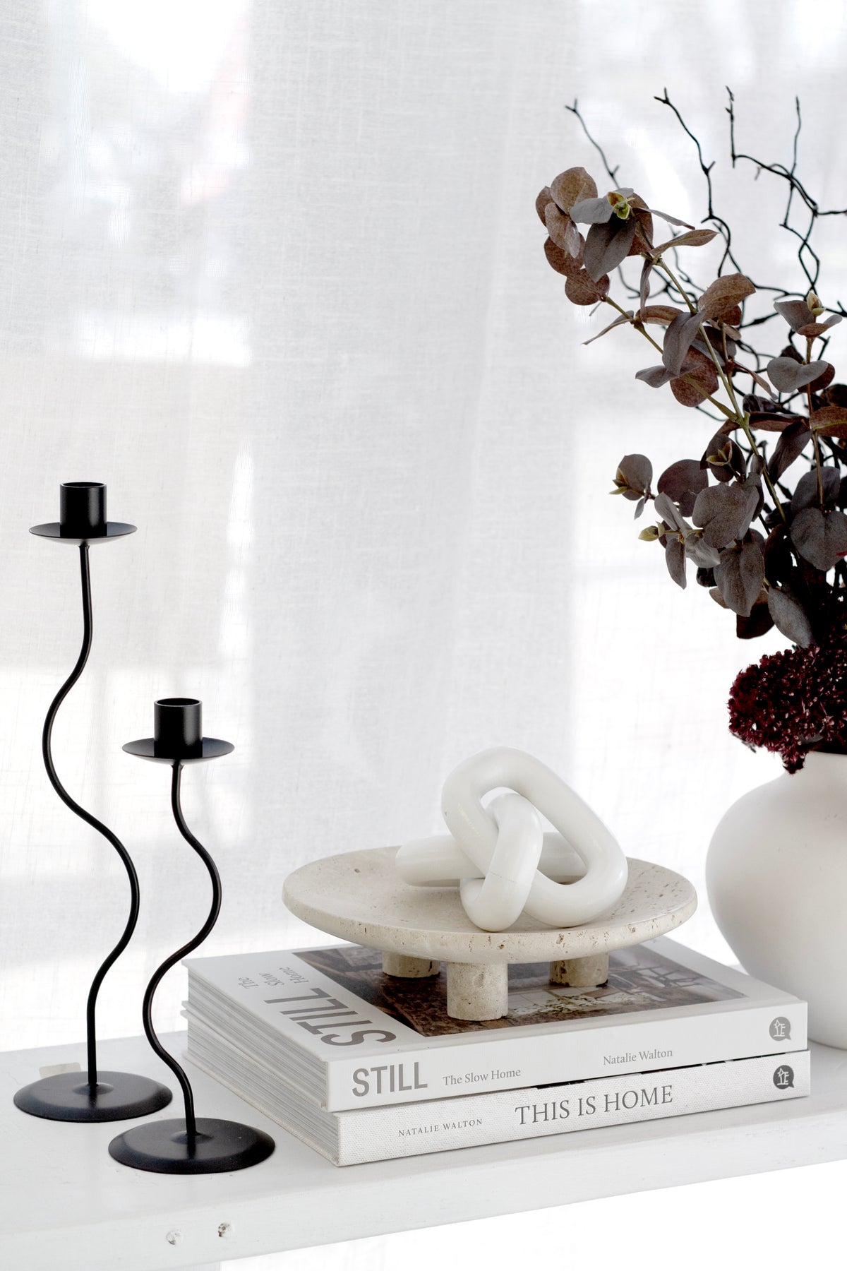 White wooden chain on a stone dish on books between two black candlesticks and dried stems