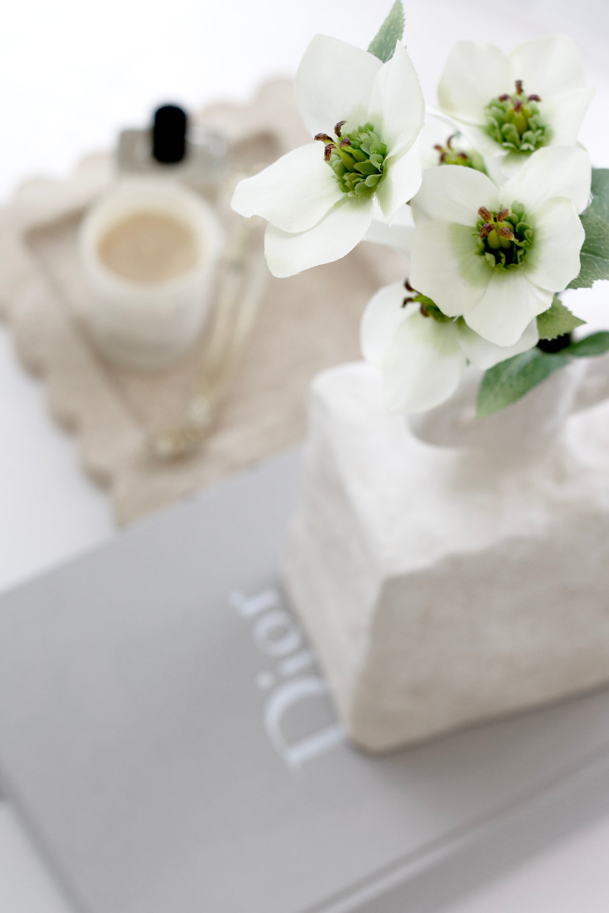 Cream hellebores in a block vase beside a candle on a book, close view