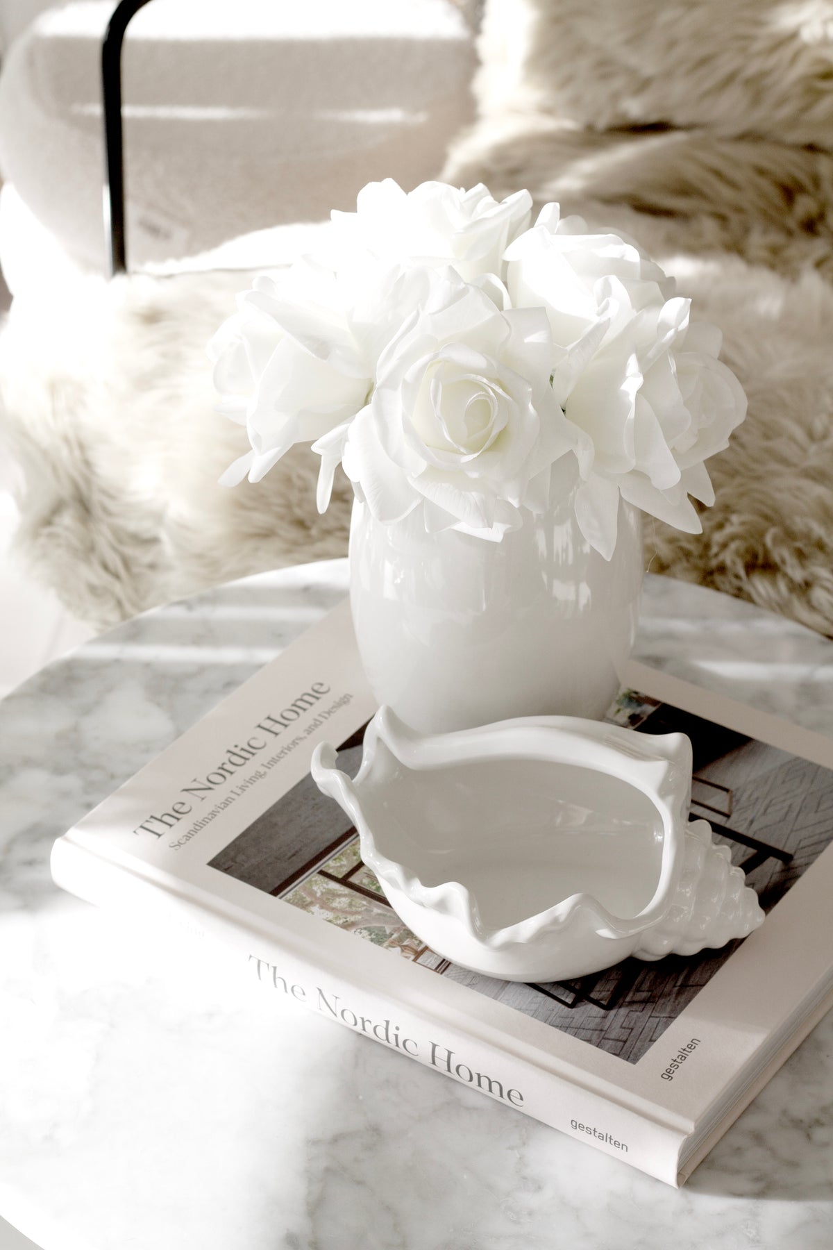 White roses in a vase on marble with the conch bowl resting on a pair of interiors books