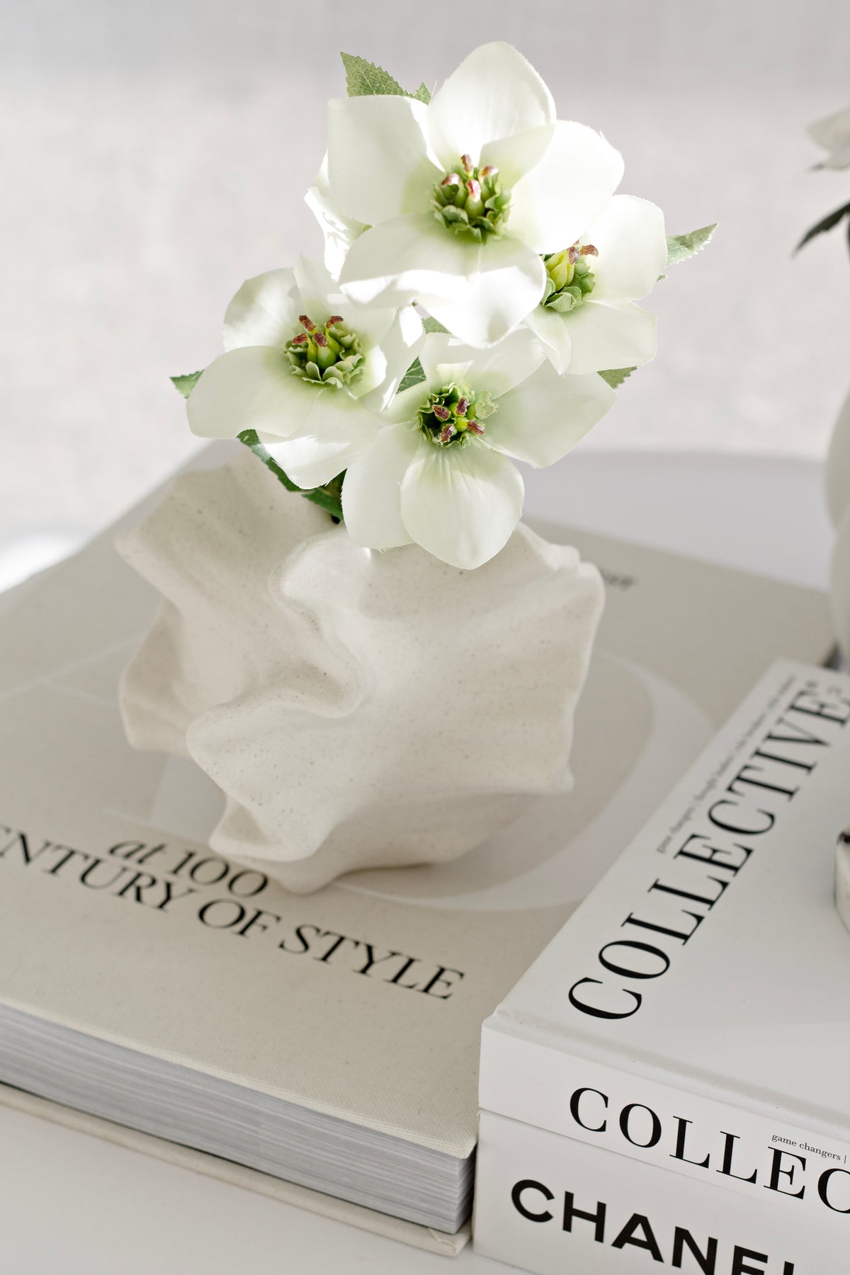 White blooms in the coral vase, set on a stack of neutral coffee table books