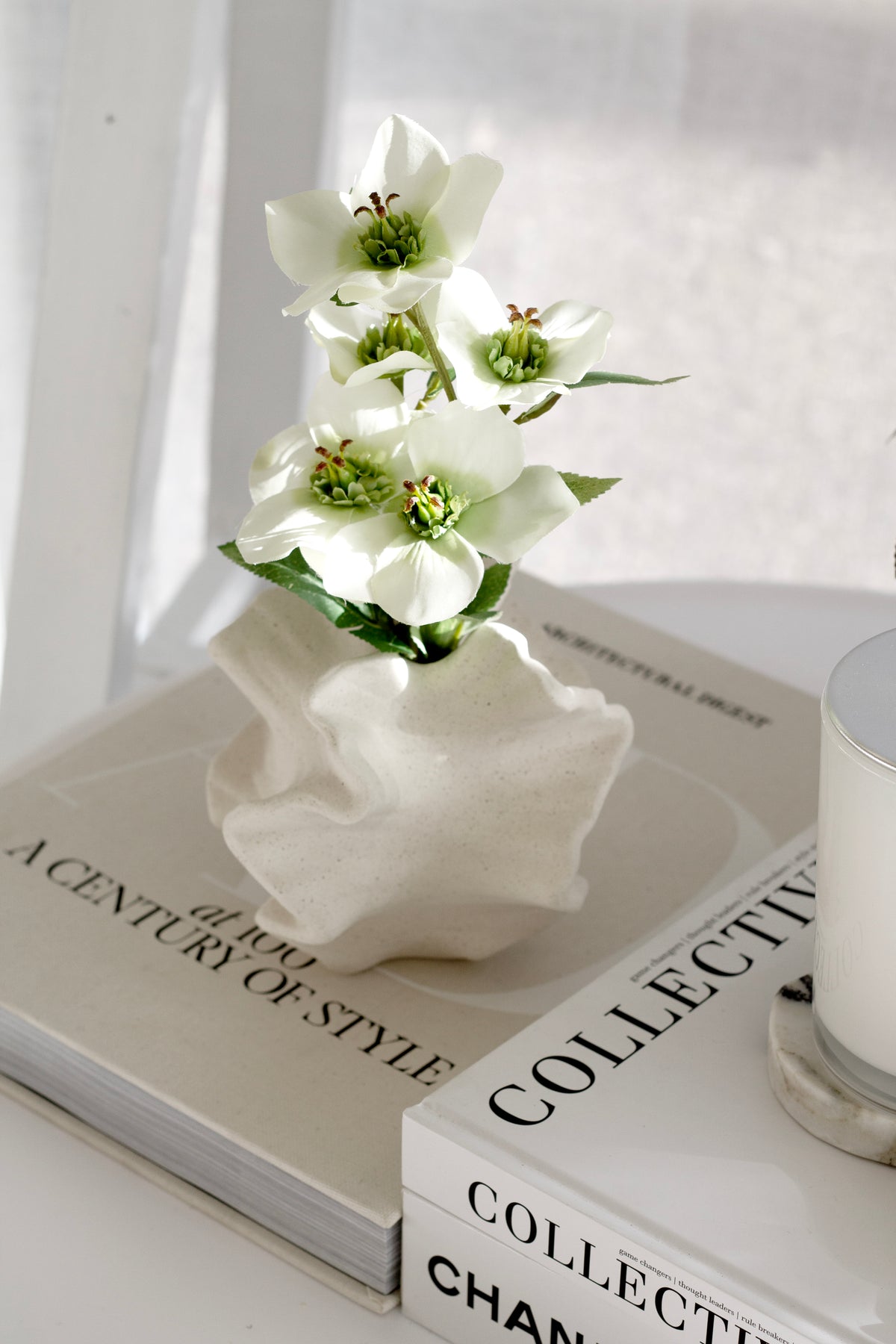White blooms in the coral vase beside a candle on a stack of style books