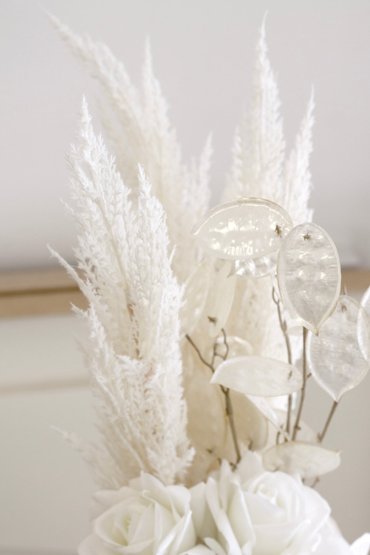 White faux toi toi plumes arranged with silvery seed pods and white roses