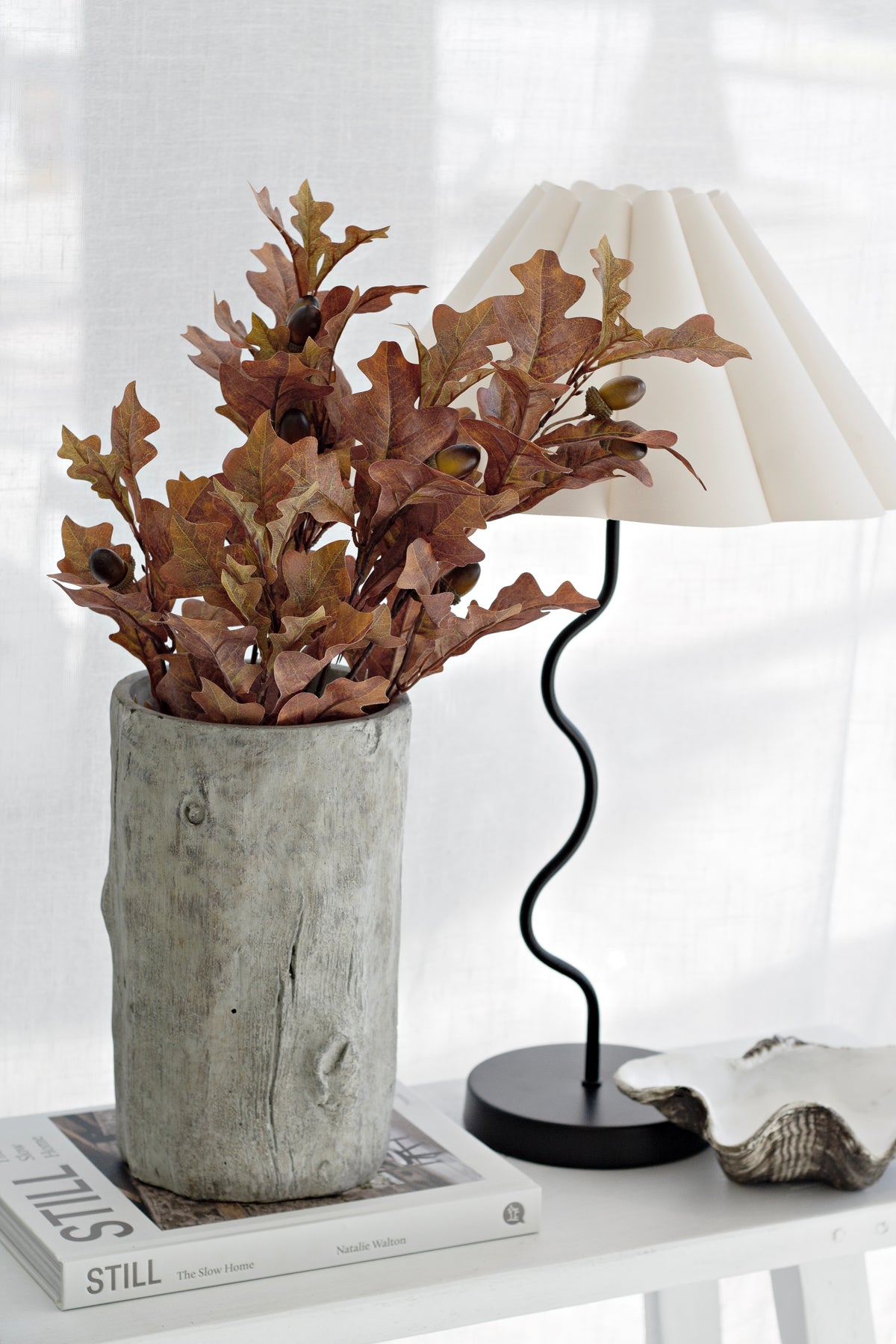 Faux oak leaf bush in a textured grey vase beside a pleated lamp with a wave base