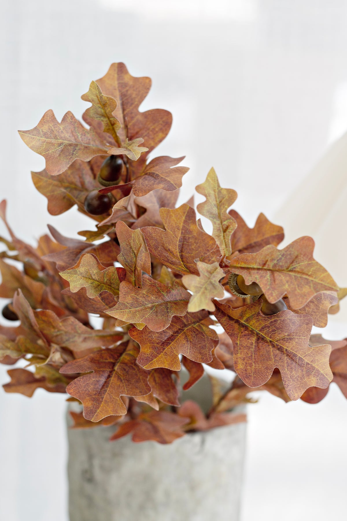Faux oak leaves and acorns in autumn tones above a grey stone vase