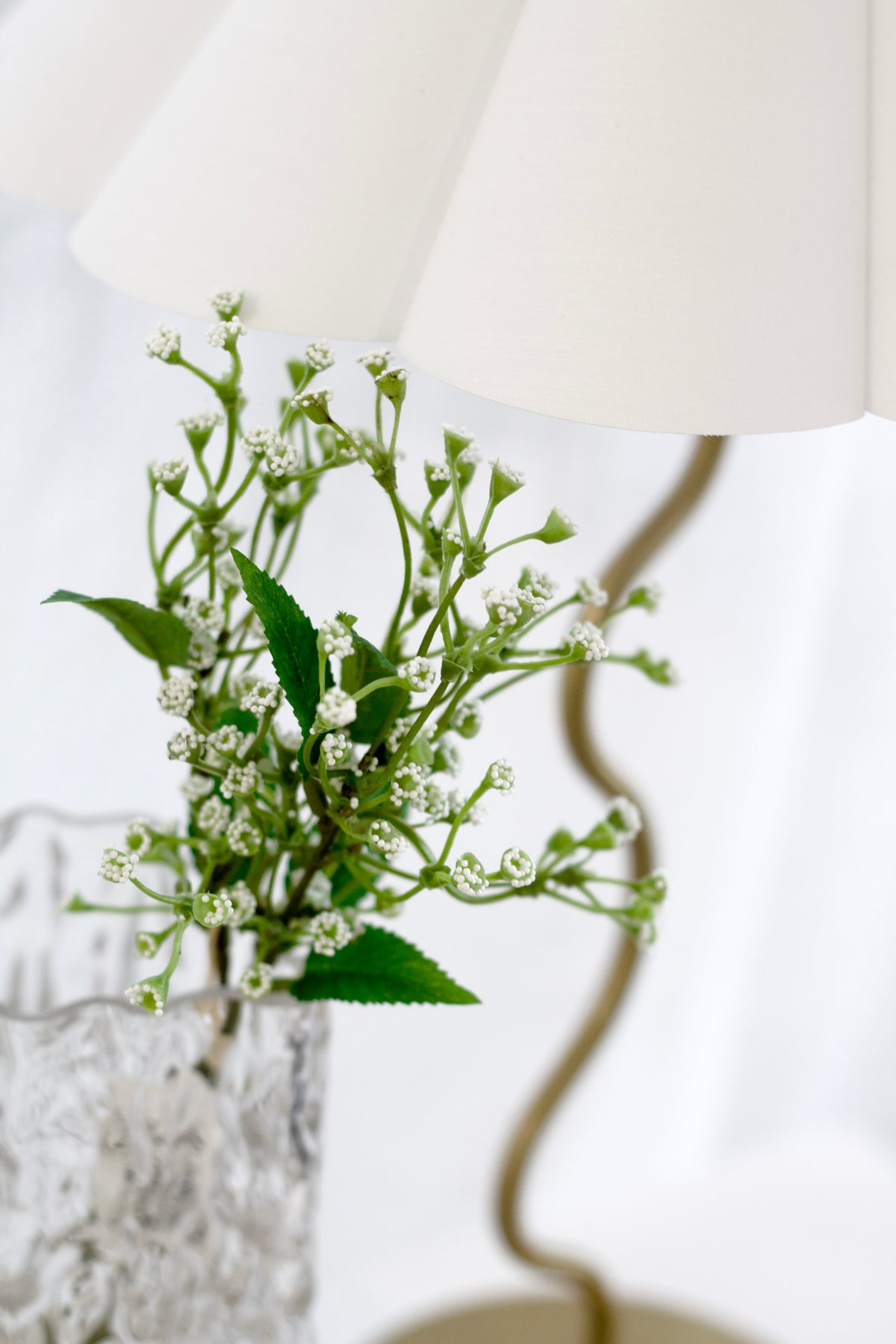 Baby's breath in a textured glass vase beside a lamp with a wavy brass base