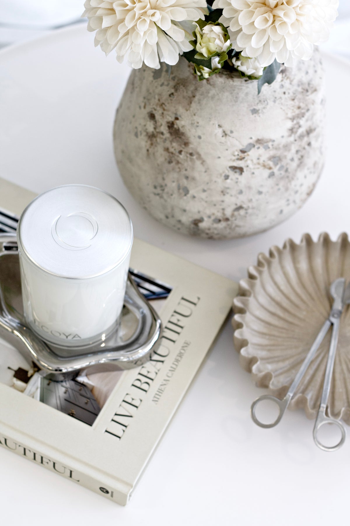 White candle on books beside a scalloped dish and wick trimmer, close view