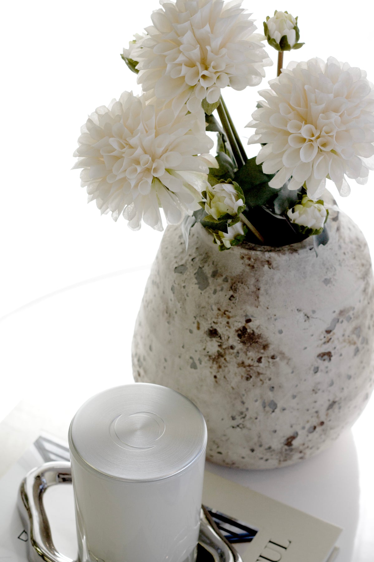 Dahlias in a rustic speckled vase beside a candle on a silver tray and a stack of books