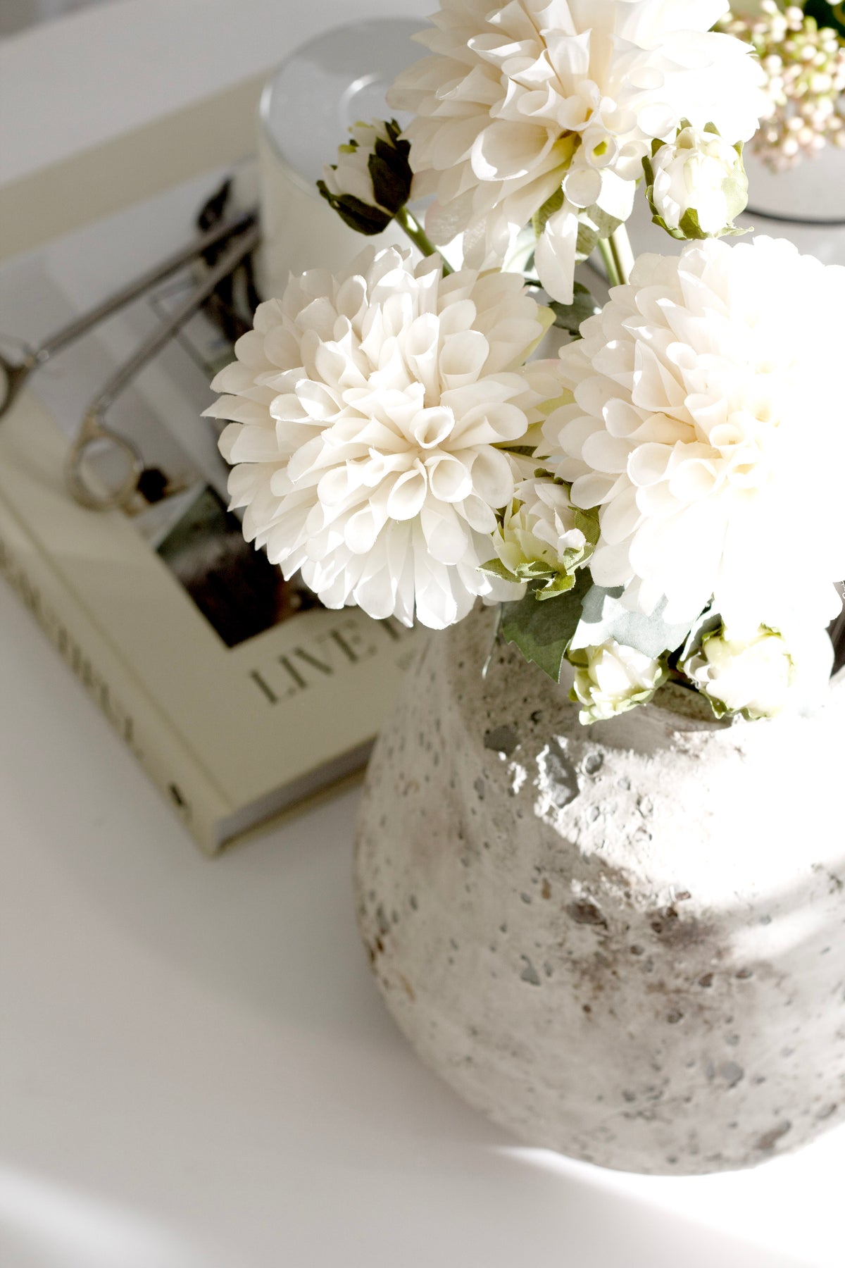 Dahlias in a speckled stone vase on a white desk beside stacked books