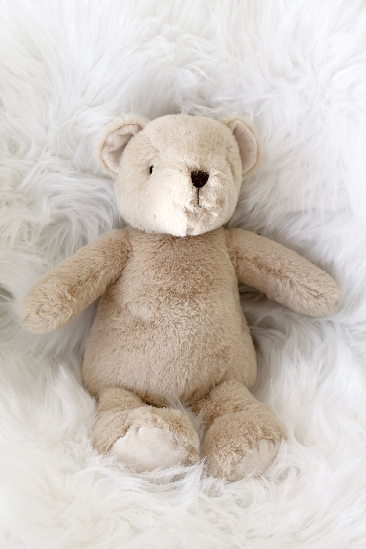 Fawn Flopsy Bear lying on white sheepskin
