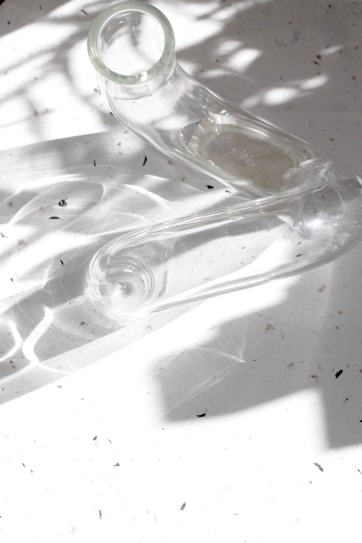Clear J-Curve vase lying on its side on a white surface under dappled sunlight