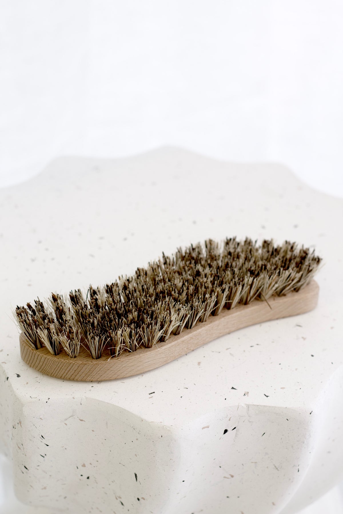 Scrubbing brush resting on a speckled white scalloped dish