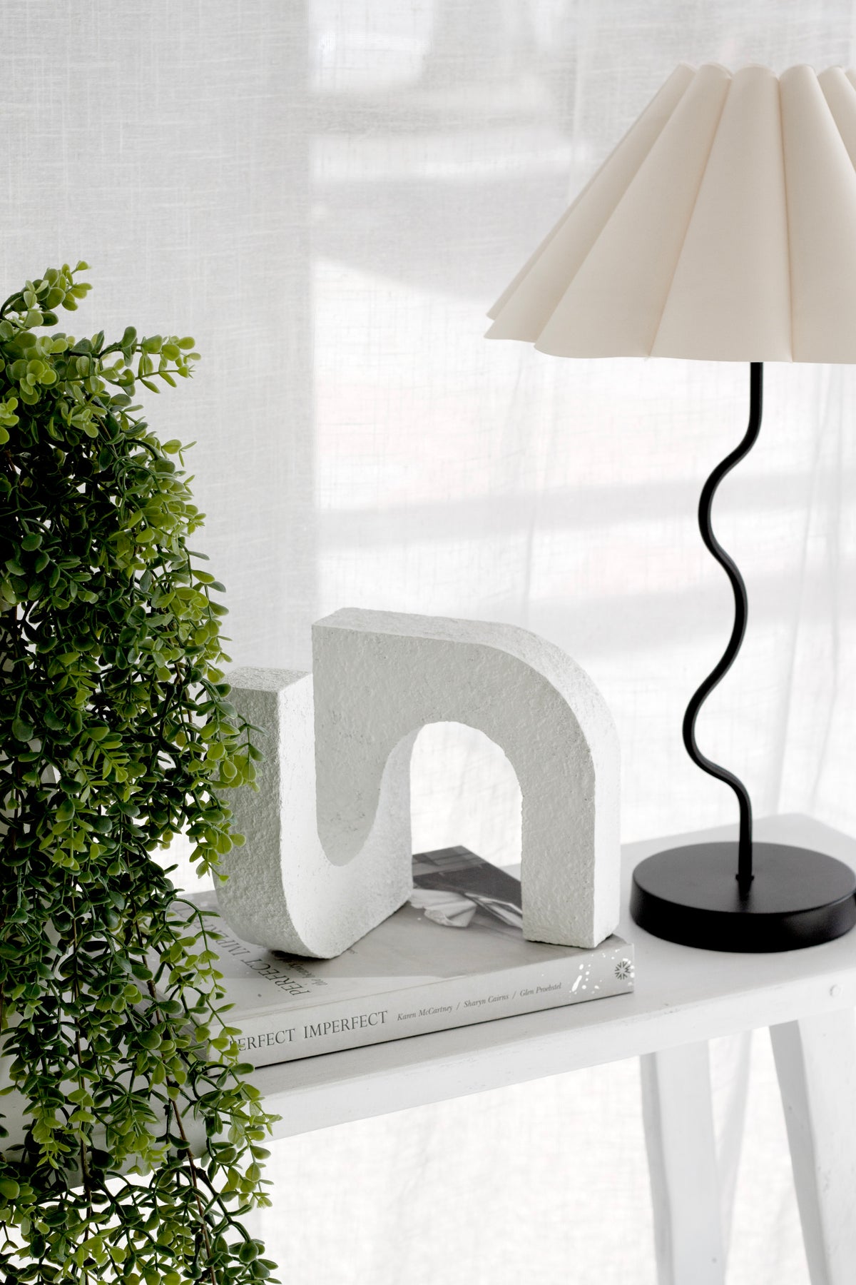 Trailing eucalyptus beside a white sculptural form and a black wavy lamp with a pleated shade