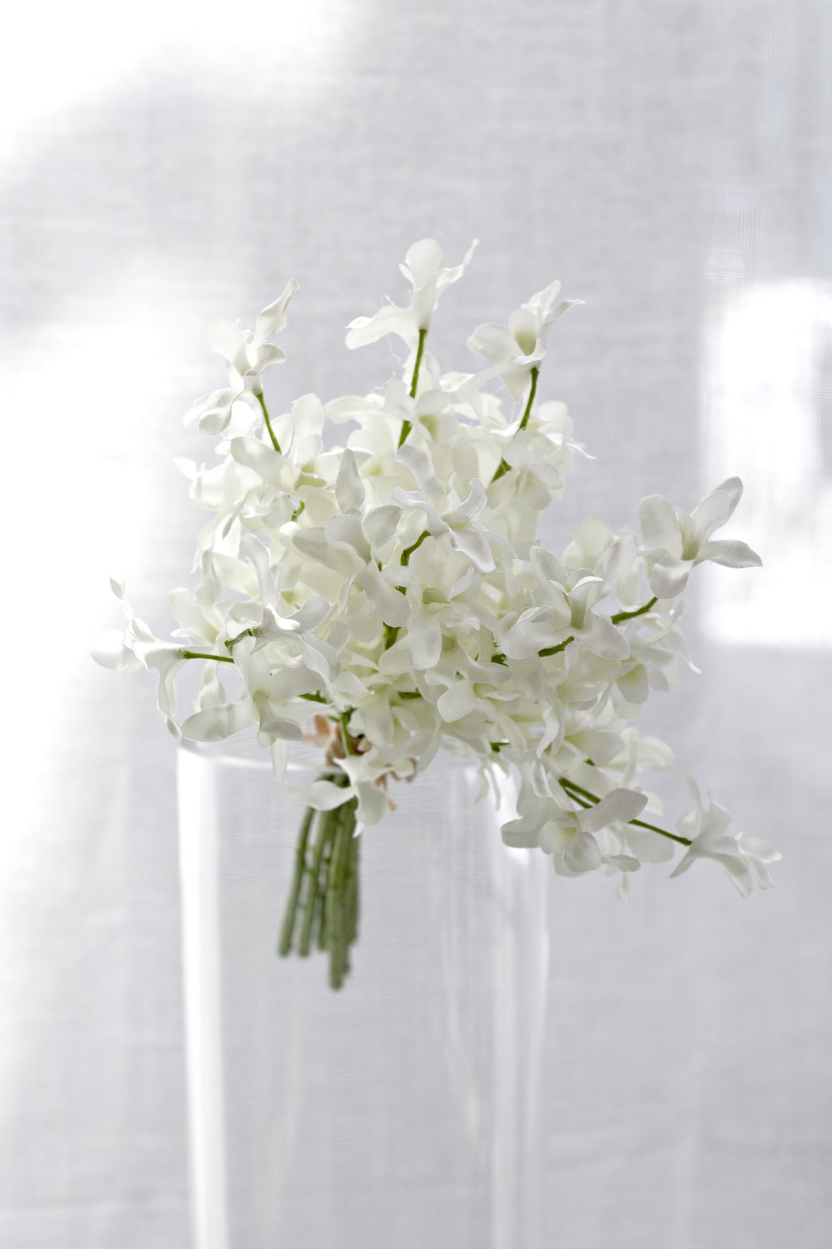 Faux orchid bundle in a slim glass vase by a window