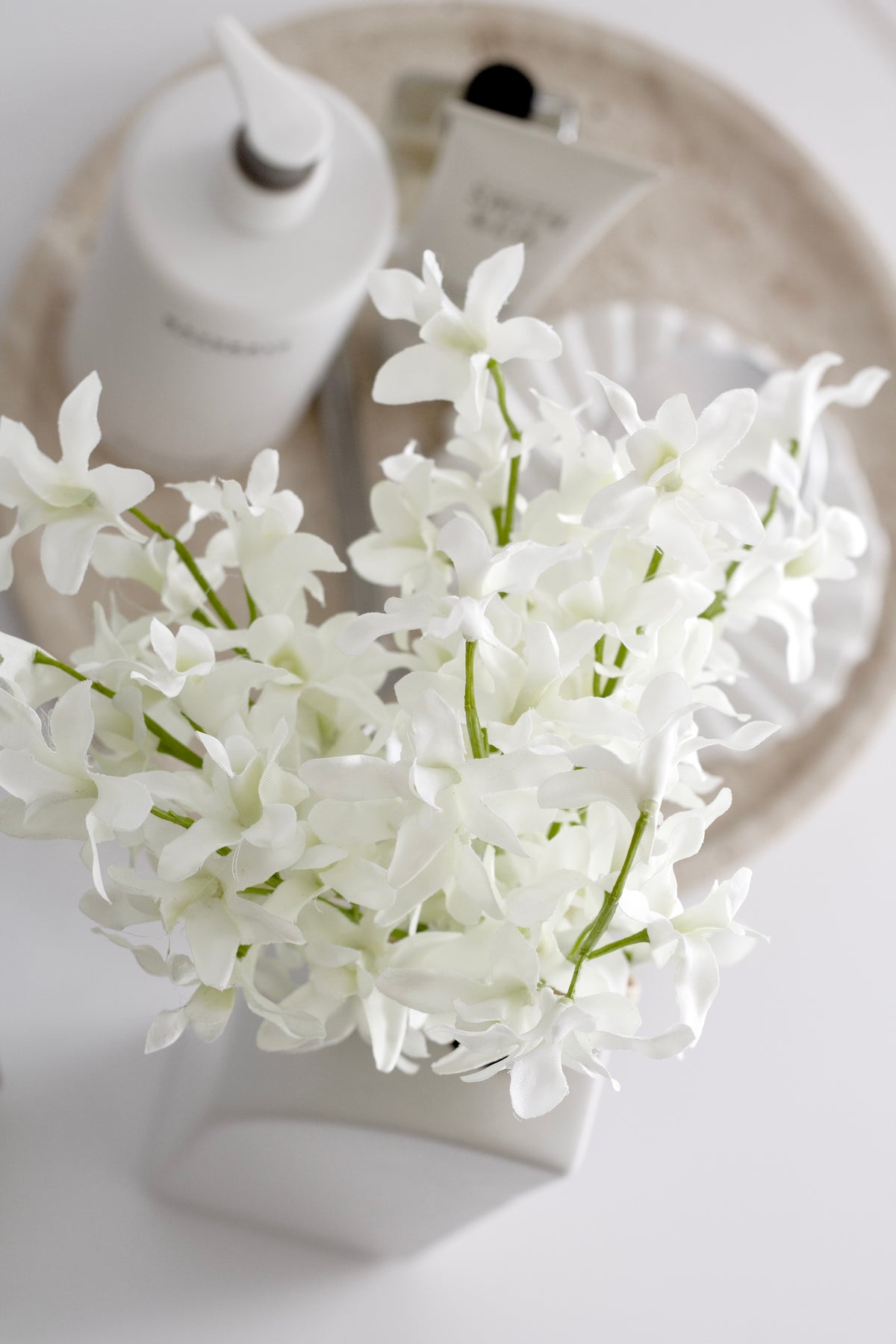 Faux white orchids in a pale ceramic vase on a marble tray