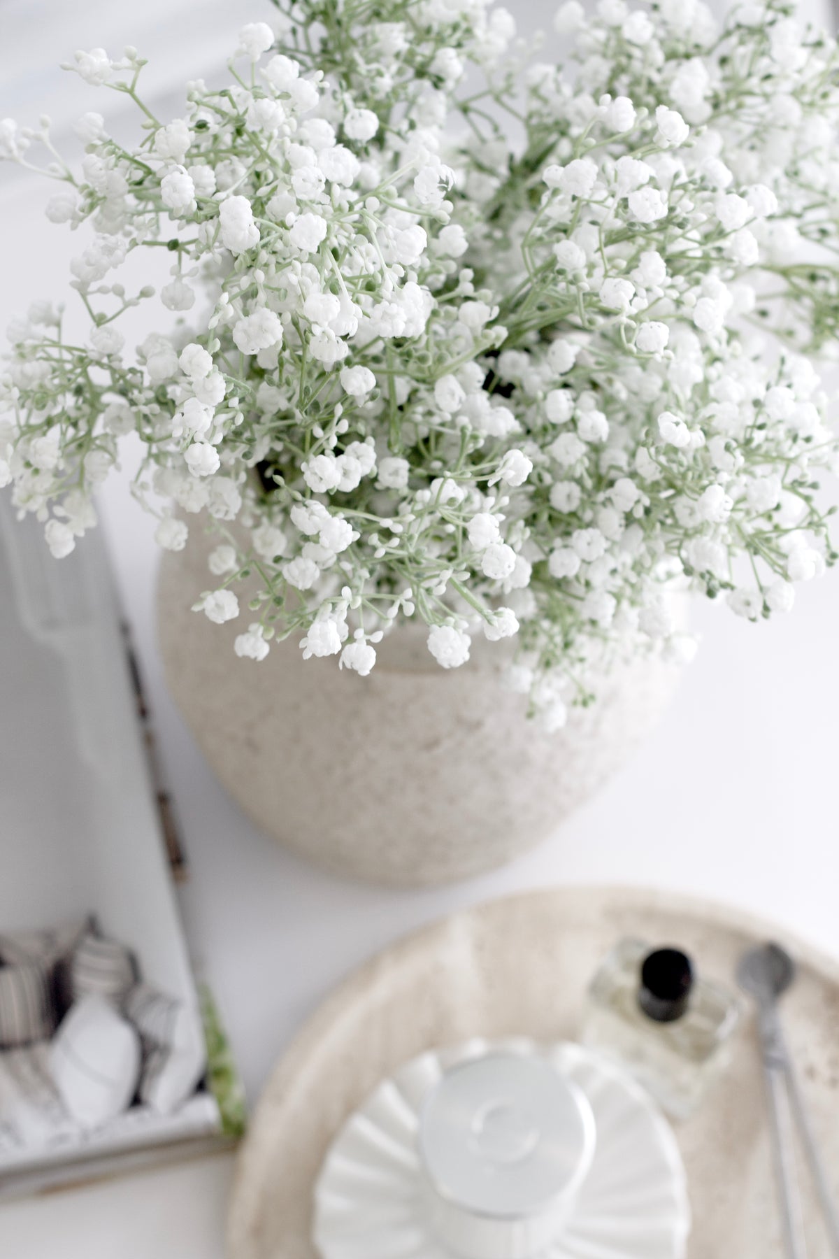 White faux gypsophila in a cream vase beside a ceramic bowl