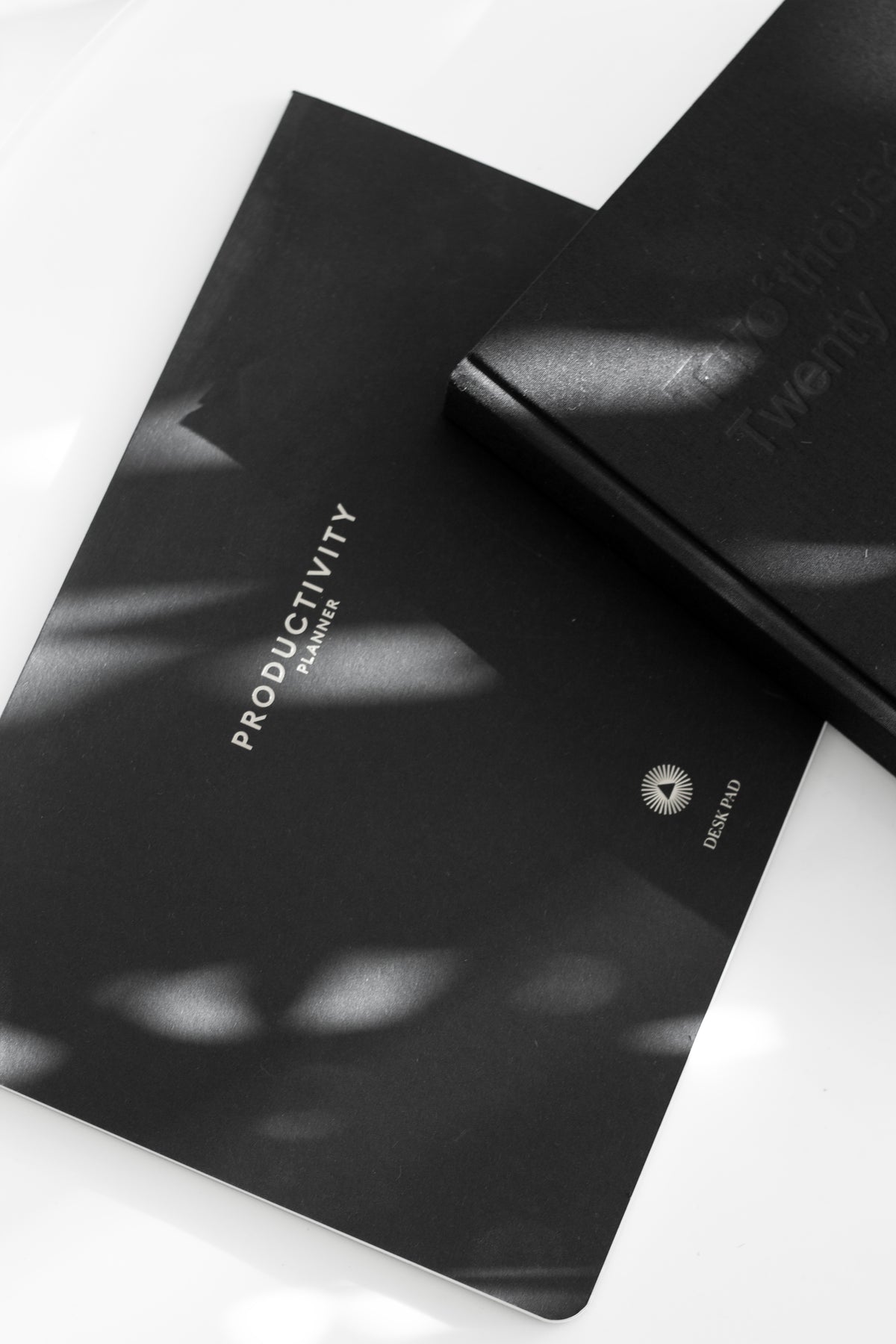 Two black Productivity desk pads in dappled light on white
