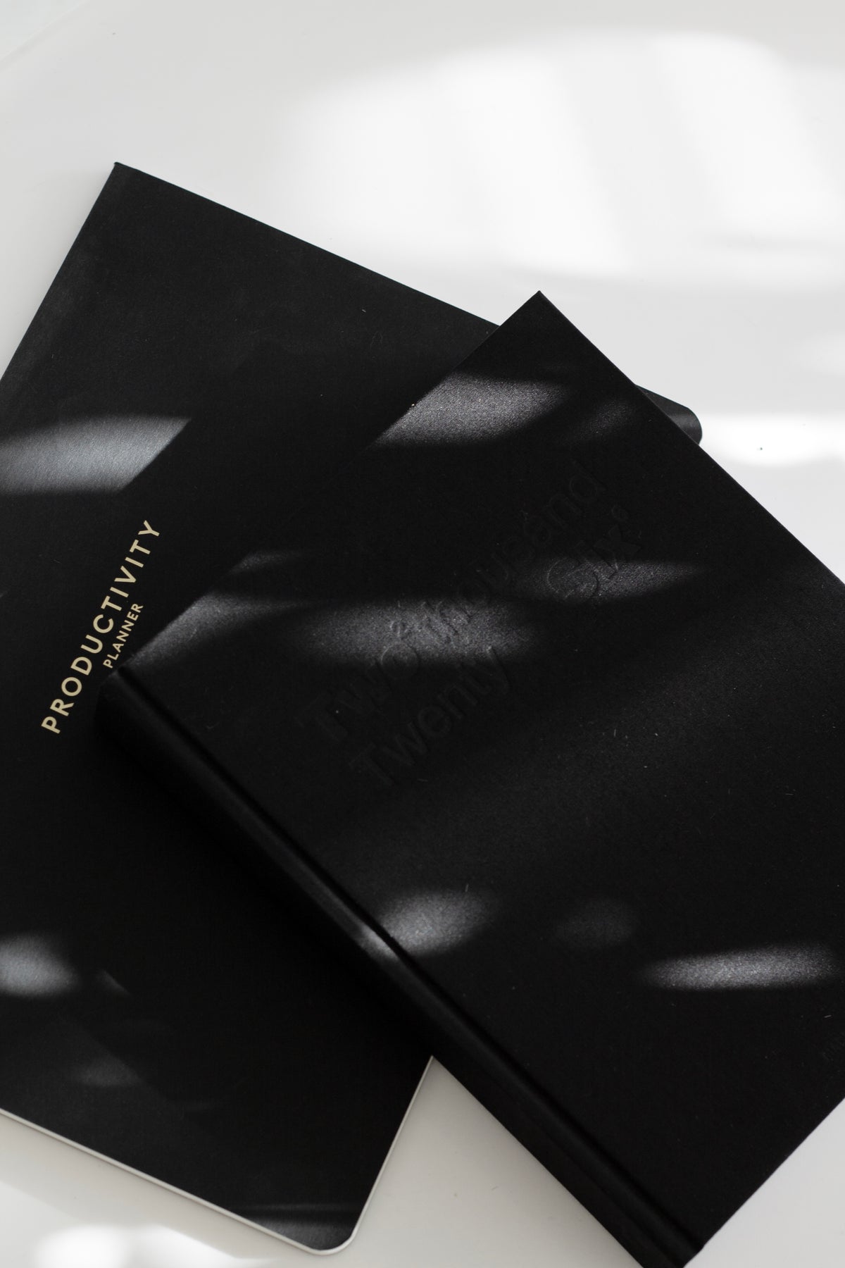 Two black Productivity desk pads overlapping in dappled sunlight