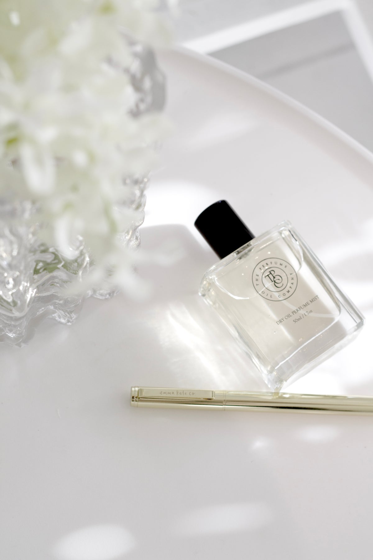 Roll-on perfume oil bottle lying on a white tray beside white blossom