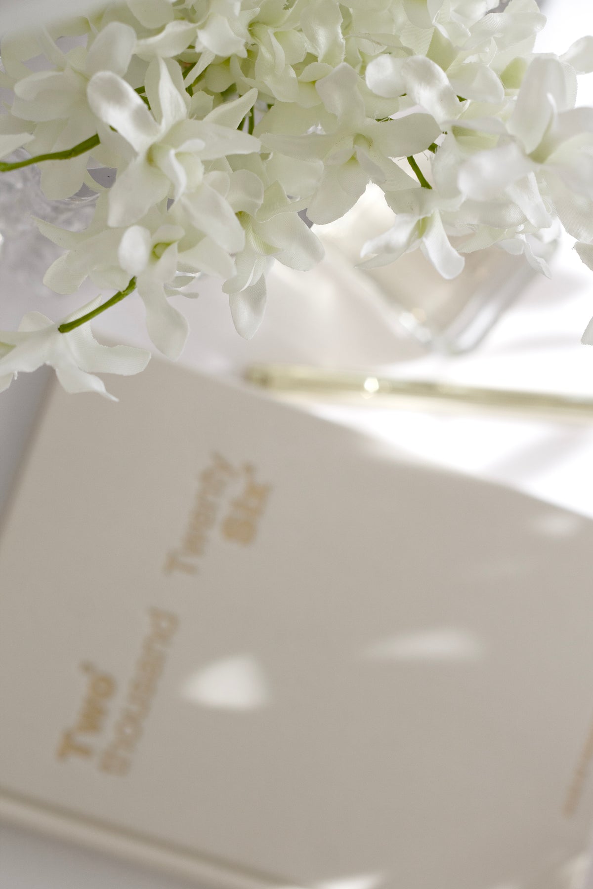 Faux orchids beside a pleated lamp and glasses on a bedside table