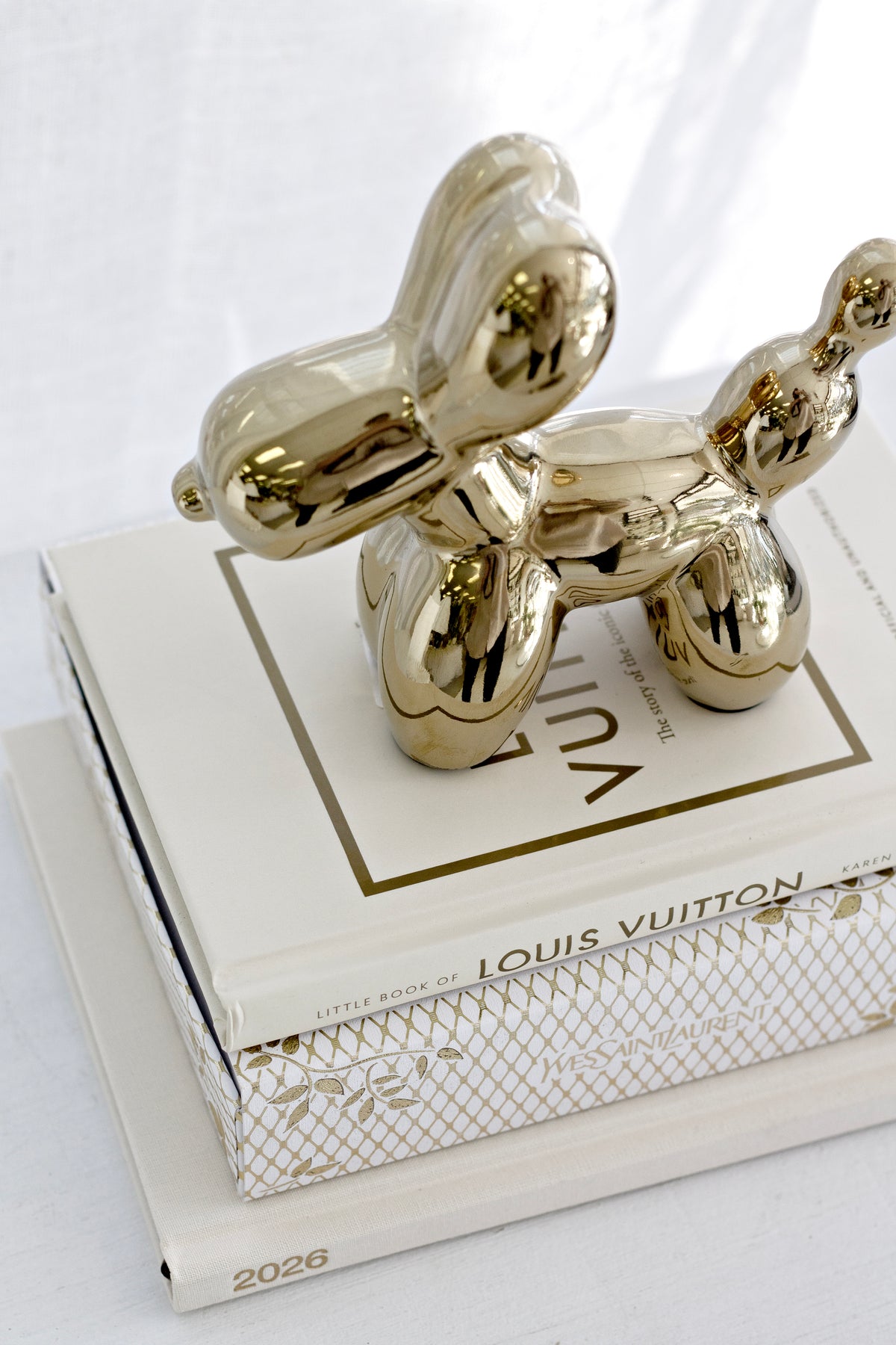 Gold ceramic balloon dog sculpture on a stack of white coffee table books