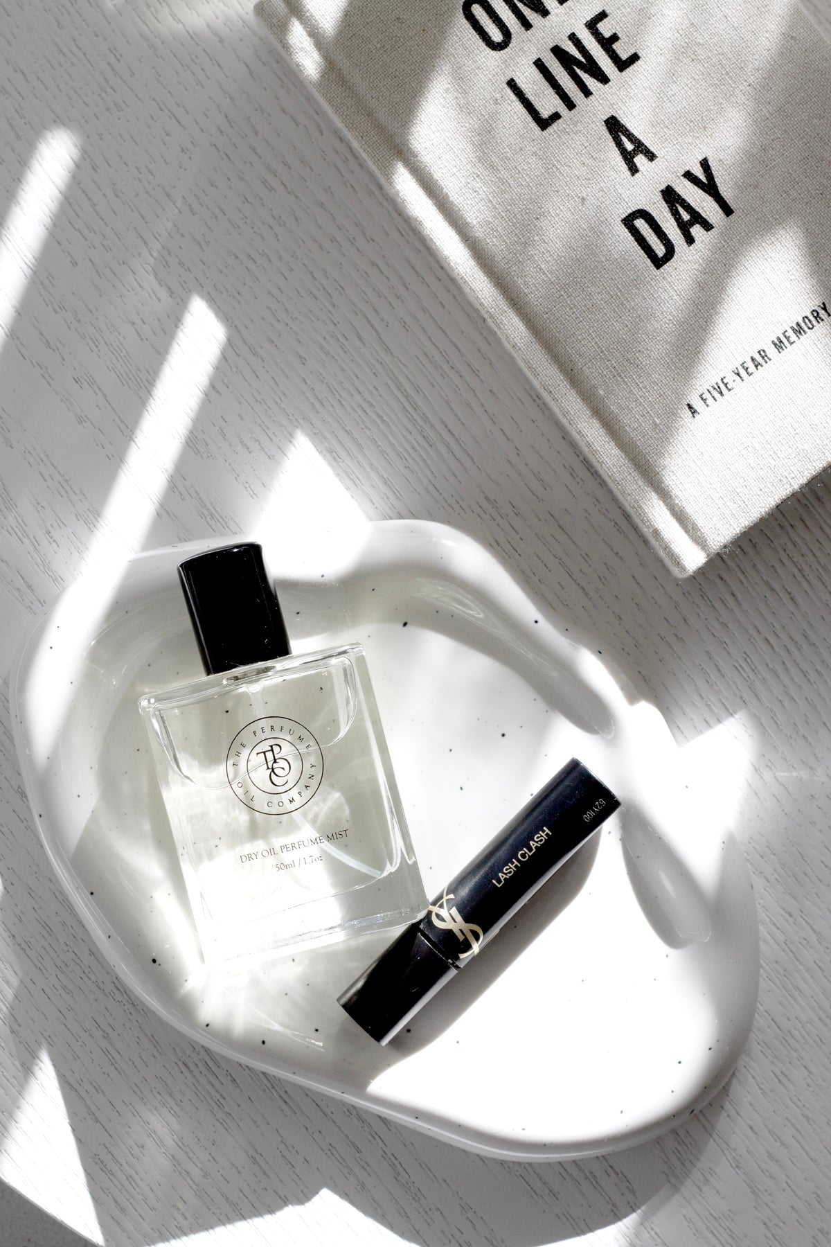 Perfume oil bottle and mist on a white dish beside a One Line a Day book