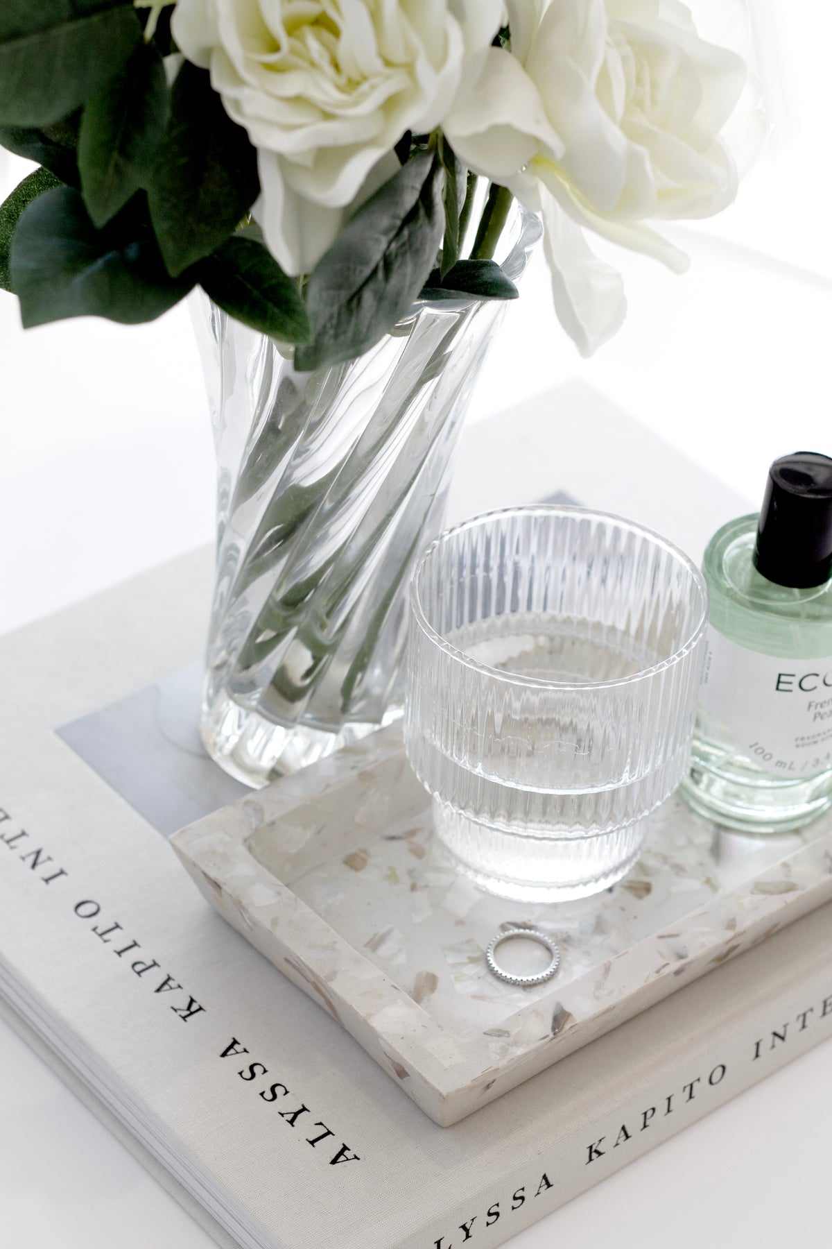 Ecoya room spray on a terrazzo tray with a ribbed glass and white flowers