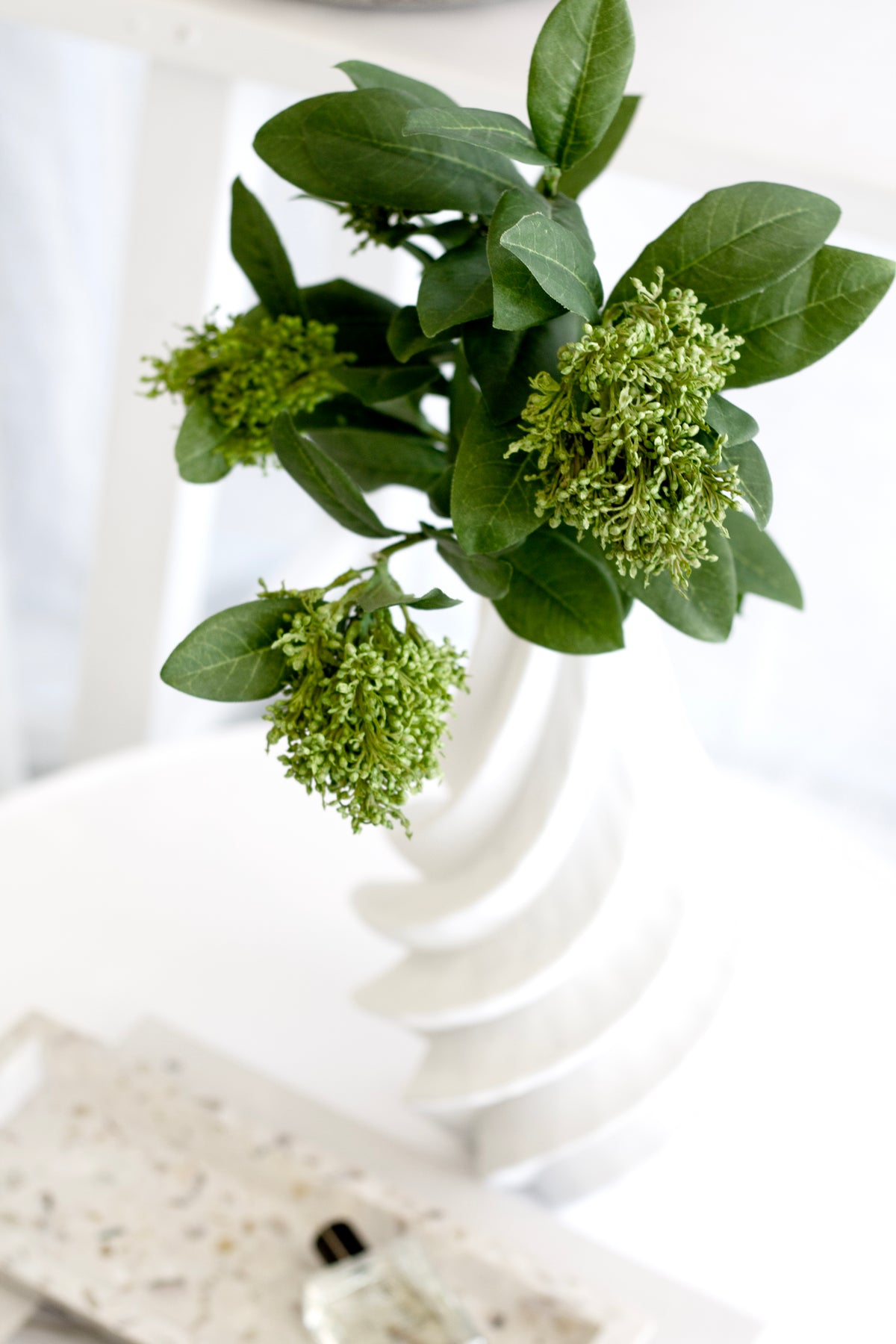Skimmia in a swirled white vase above a terrazzo tray and perfume