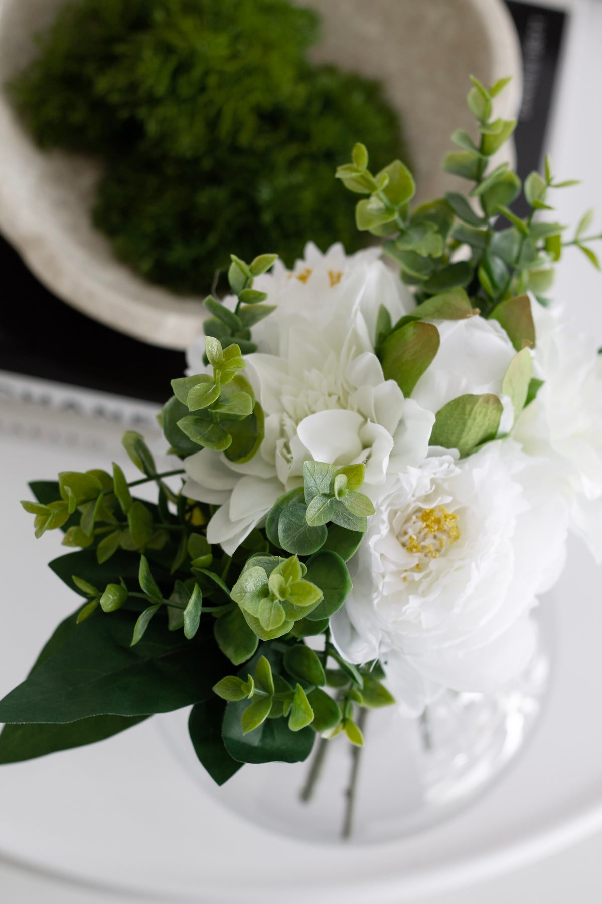 Bouquet in a glass vase beside a bowl of moss, seen from above