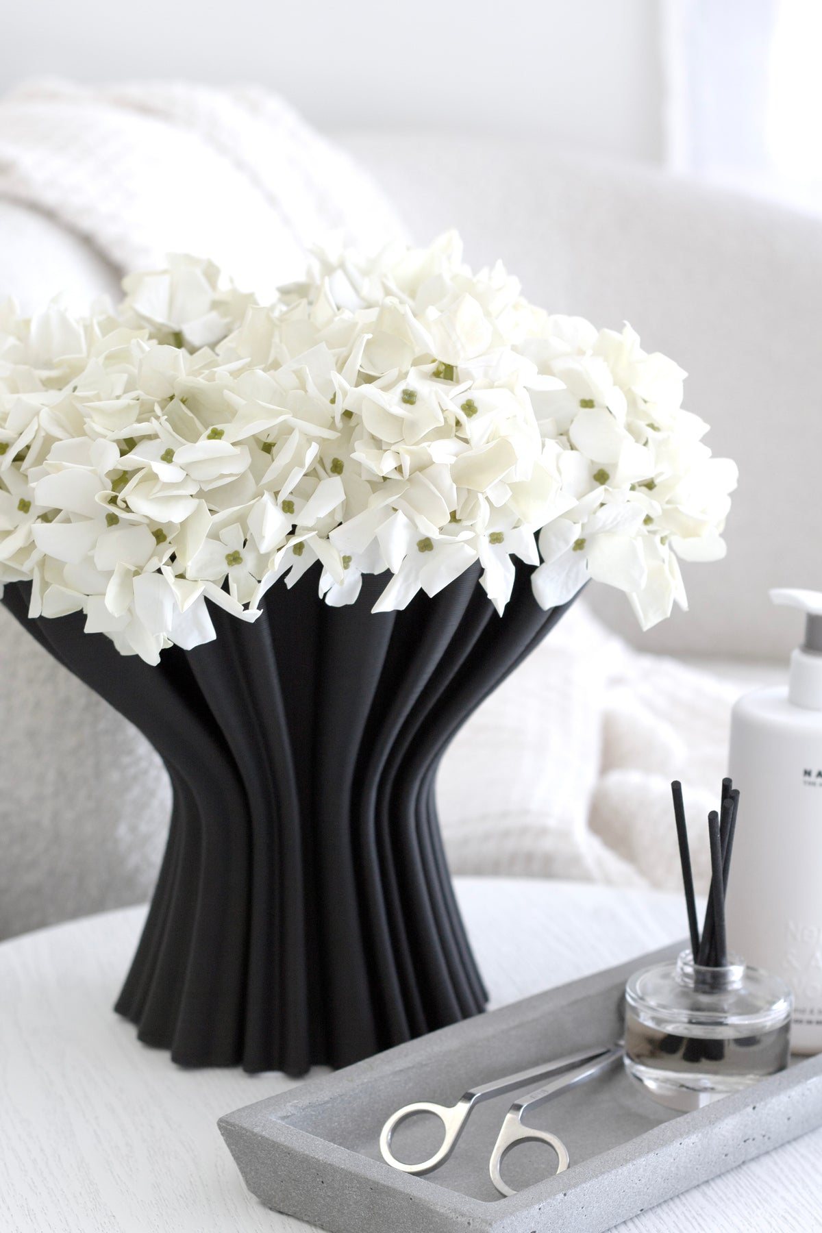 Zakkia concrete tray holding a reed diffuser and wick trimmer beside a black vase of white hydrangeas