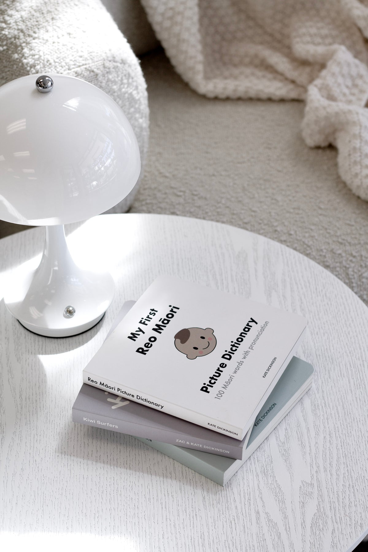 My First Reo Māori Picture Dictionary on a round white table beside a white lamp and a knit throw