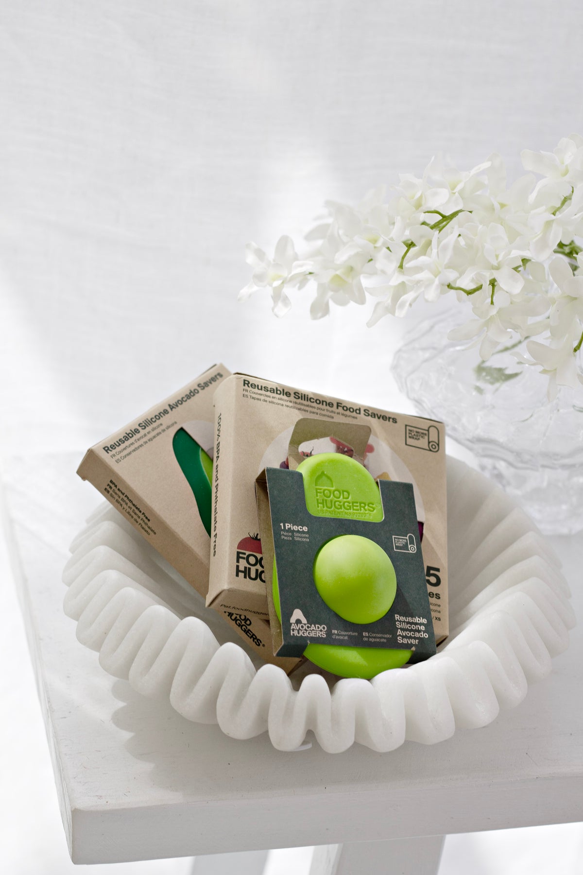 Food Huggers and Avocado Huggers packs in a white ruffled dish, with white blossom behind
