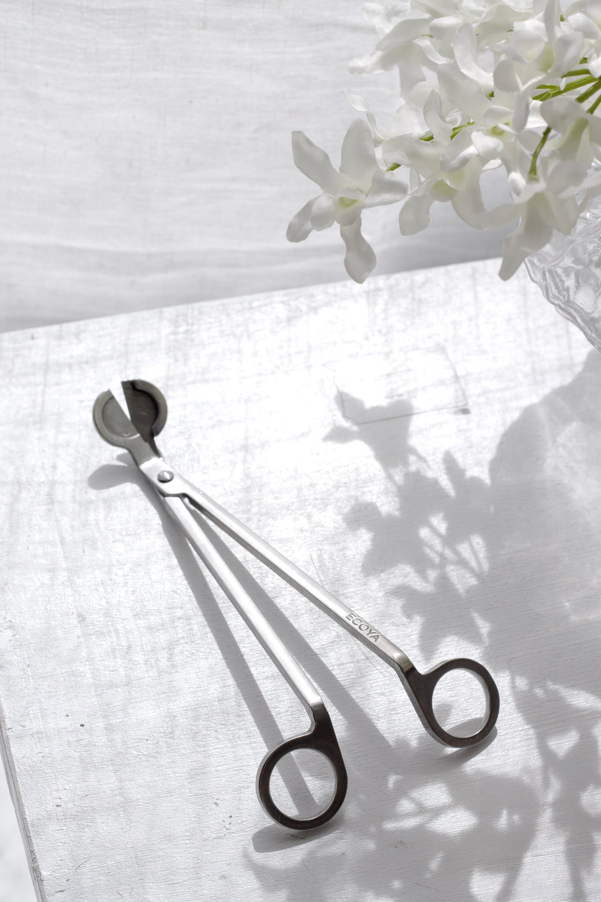 Wick trimmer on white linen in soft leaf shadow