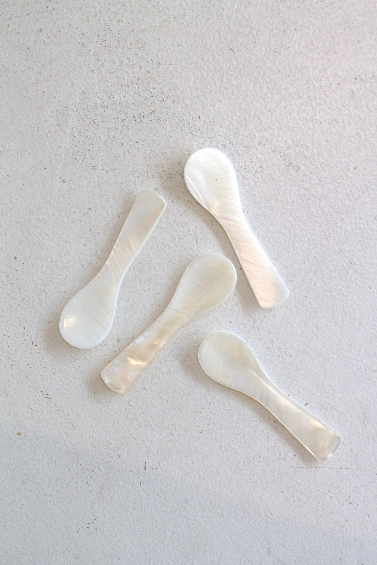 Four mother of pearl spoons scattered on a pale surface