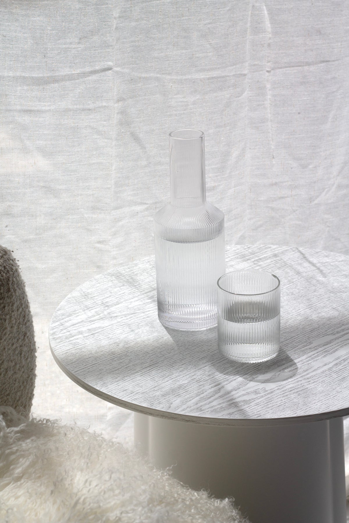 Amalfi decanter and glass on a round white side table against a sheer curtain