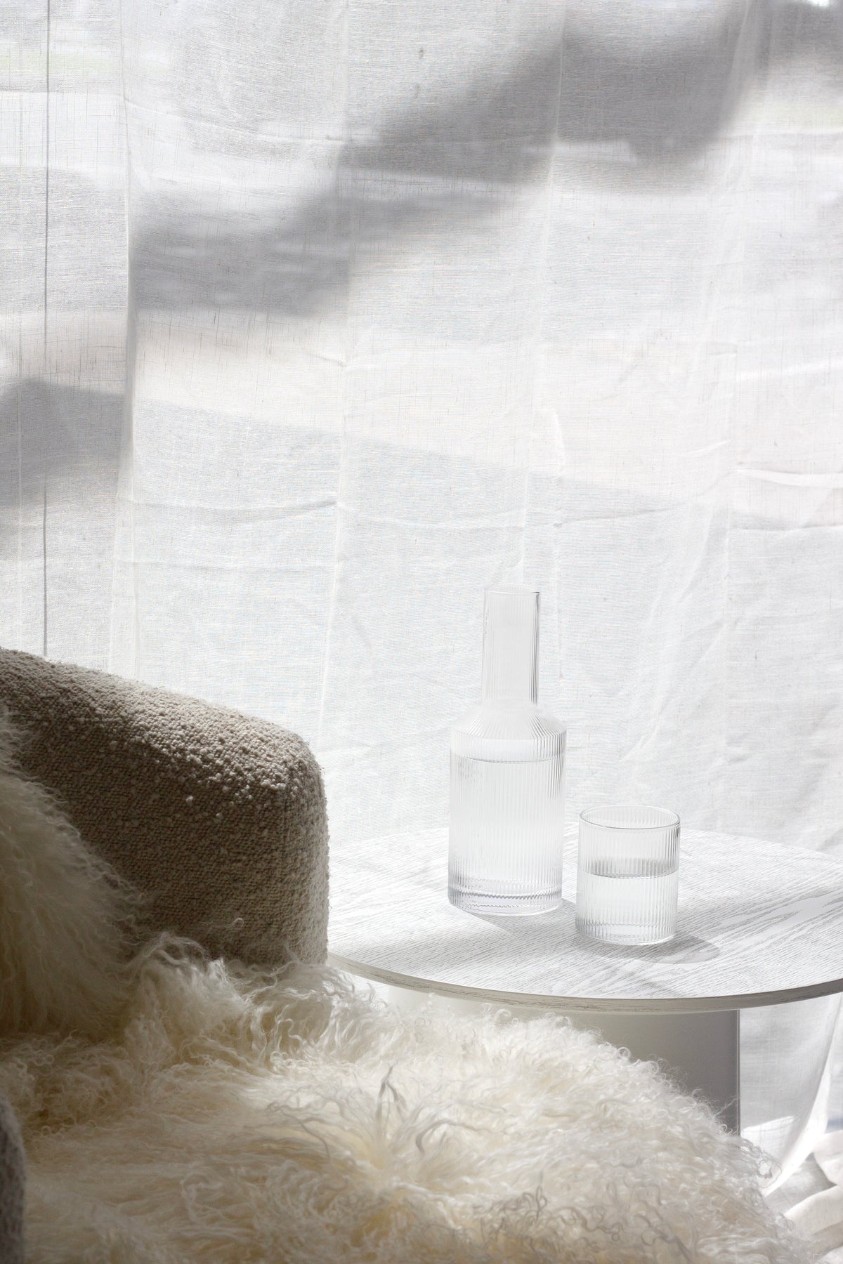 Decanter and tumblers on a side table beside a sheepskin in soft daylight