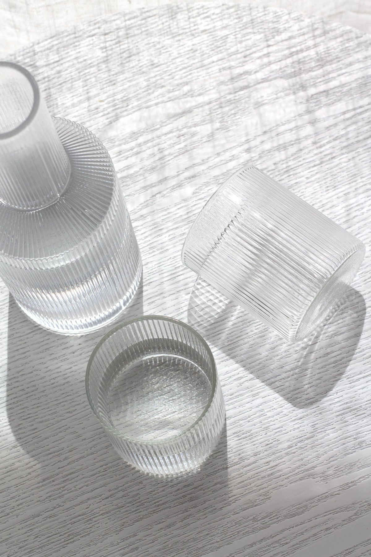 Fluted decanter lying on its side with two tumblers on white linen