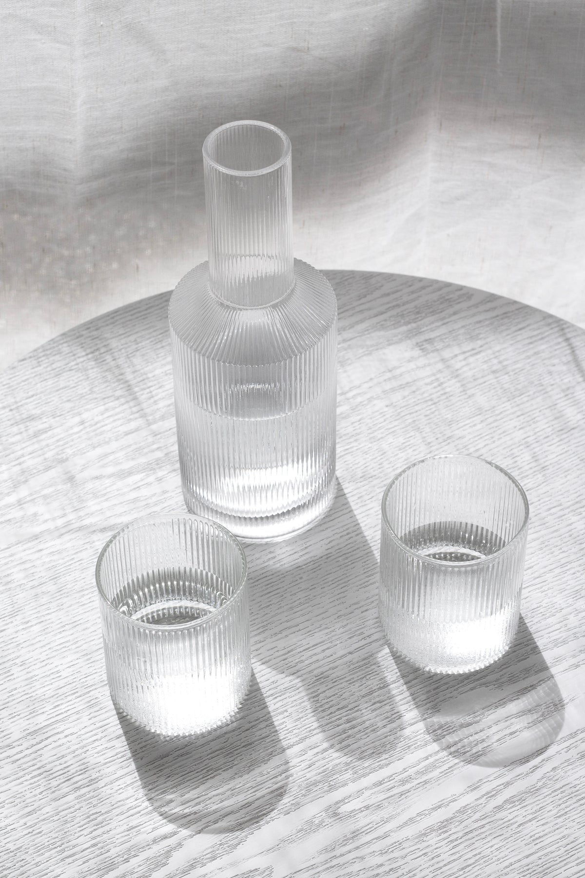 Amalfi decanter and two fluted glasses on a round table in afternoon shadow