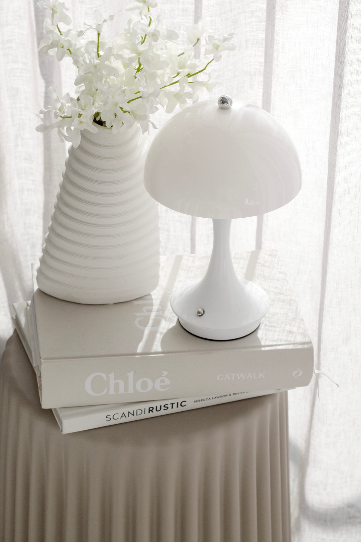 Nude ribbed stool with a ribbed vase of white flowers and a mushroom lamp resting on two books