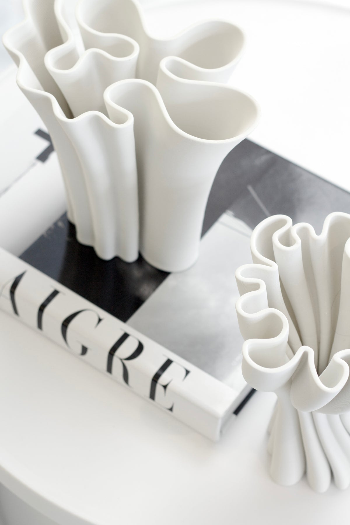 Two white Cooper 3D printed vases with ruffled openings on a stack of monochrome books
