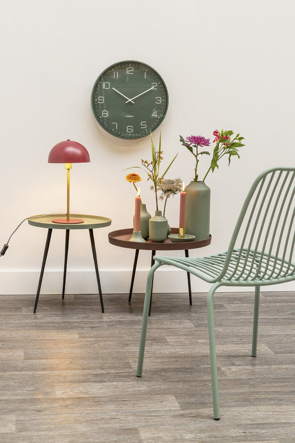Karlsson Lofty Wall Clock in matte green above side tables with a red lamp and flowers
