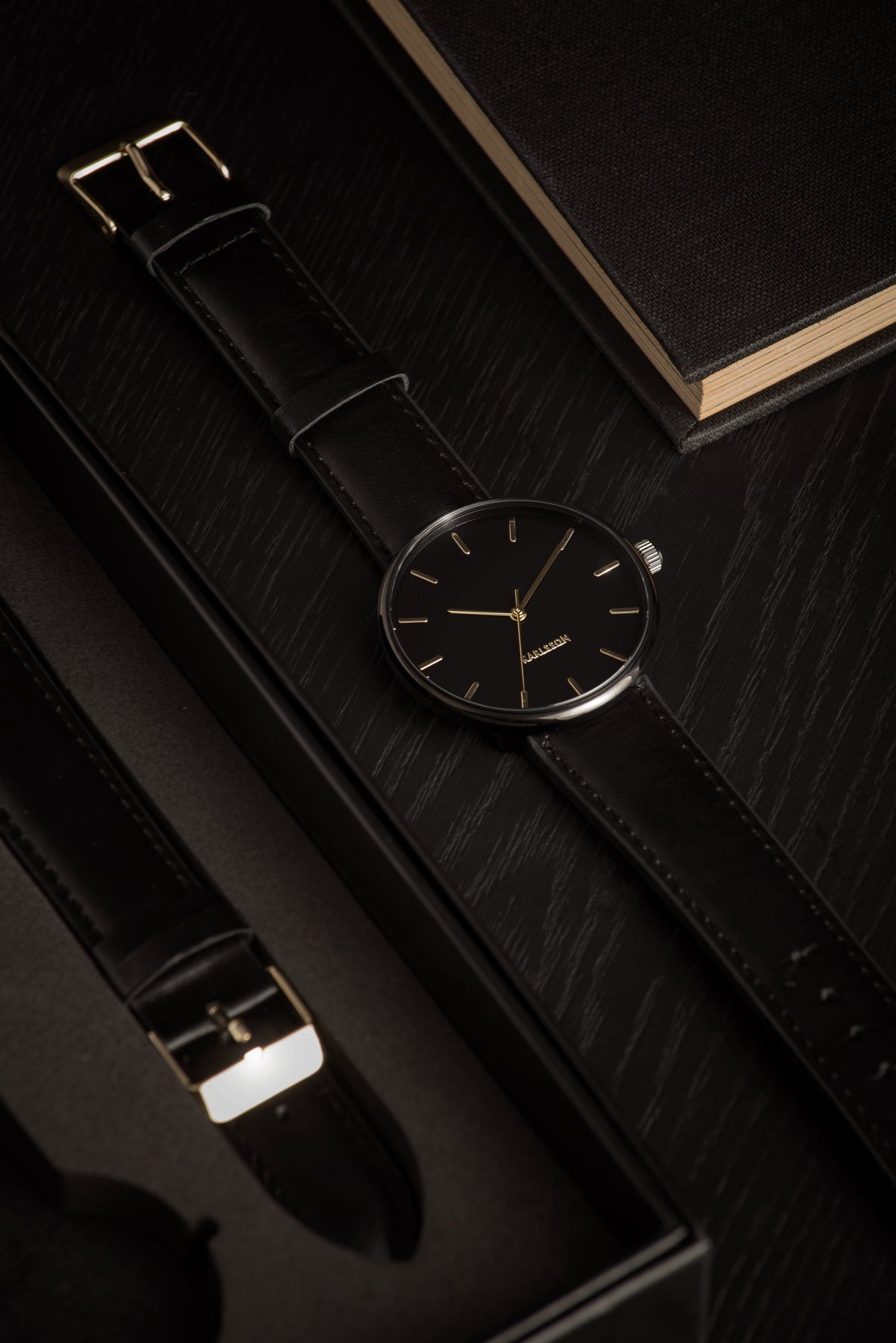 Karlsson Minimal watch in black on a dark surface beside a spare strap and a black notebook