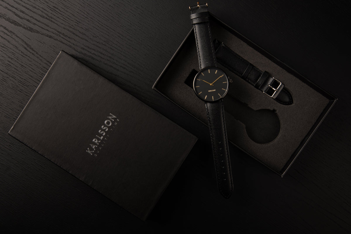 Karlsson Minimal watch in black in its open gift box on a dark surface with the lid alongside
