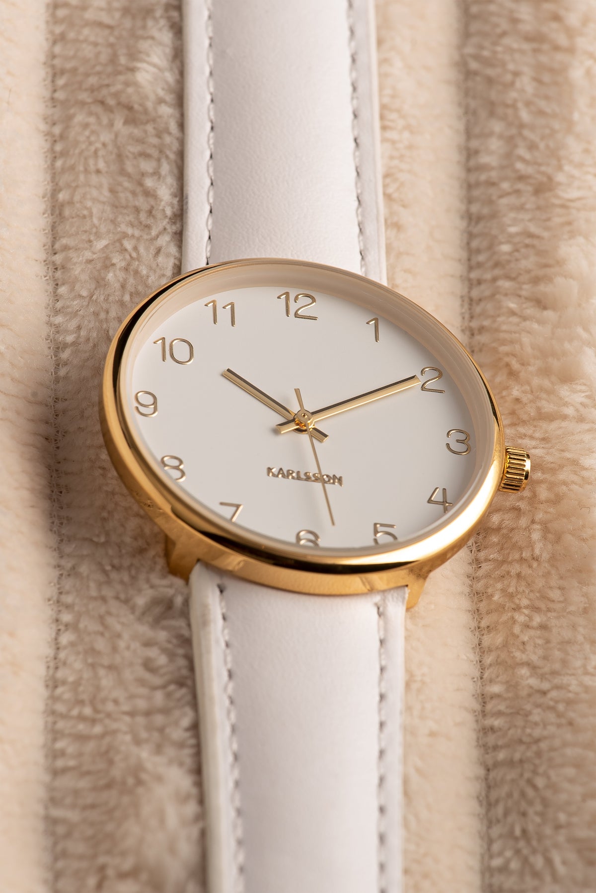 Close up of the Karlsson Charm watch face and gold numerals on beige fabric
