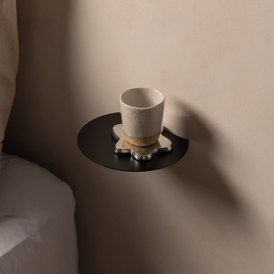 Close-up of a black FOLD Round Shelf holding a ceramic cup on a coaster
