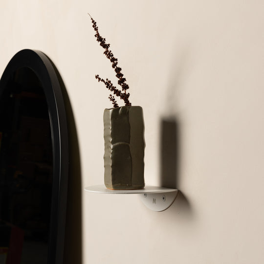 Small white FOLD Round Shelf with a vase of dried stems beside an arched mirror, wider view
