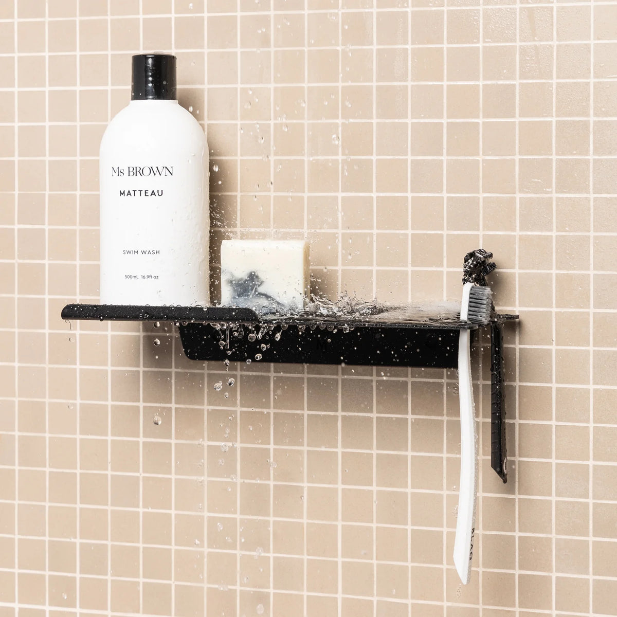 Black FOLD shower shelf with a bottle and toothbrush on blush pink tiles
