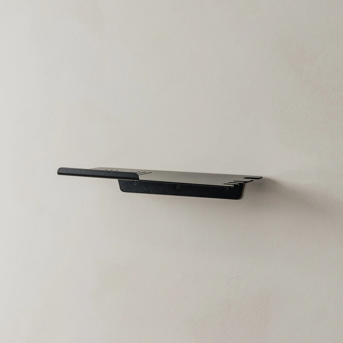 Empty black FOLD shower shelf mounted on a grey wall