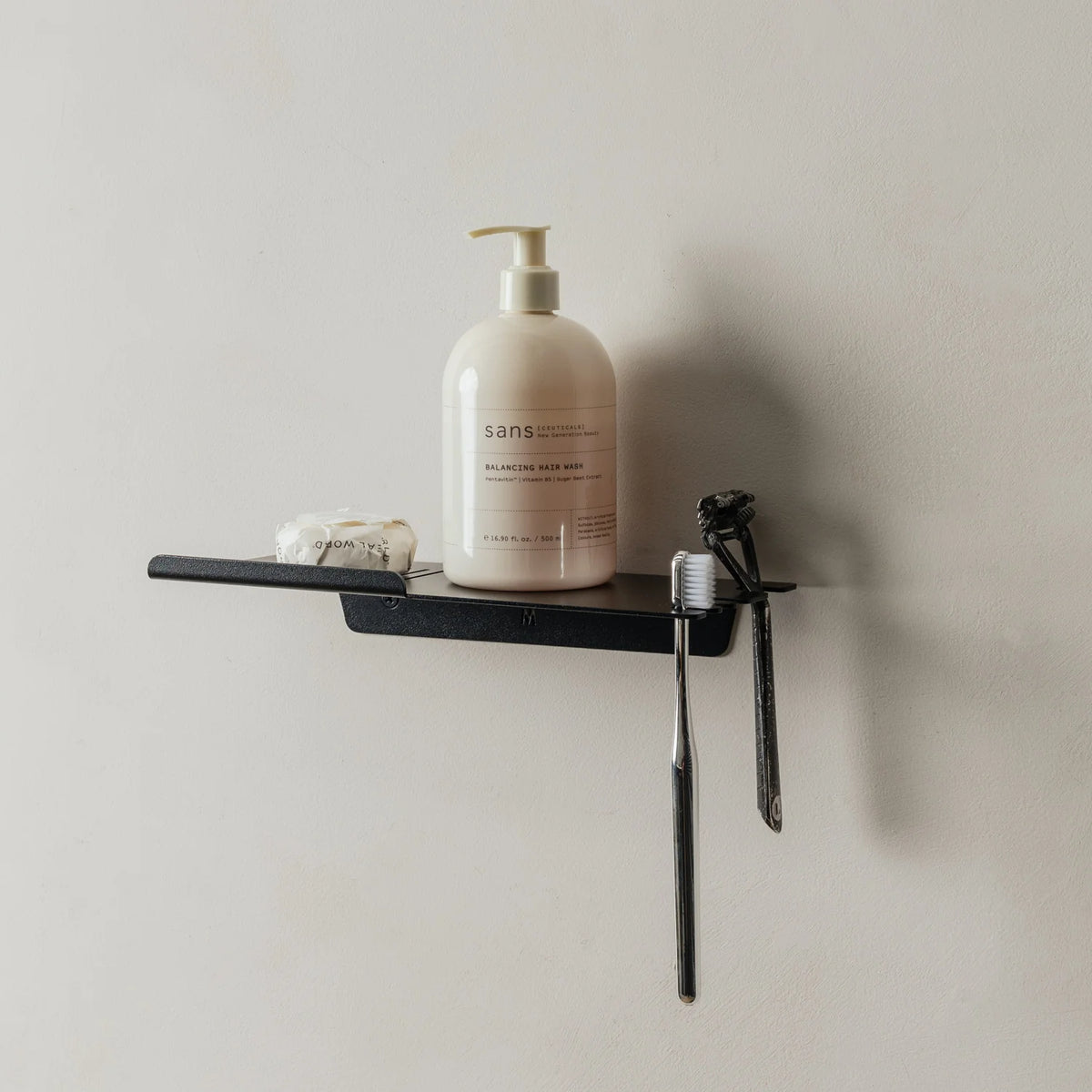 Black FOLD shower shelf with a bottle and razor on a grey wall