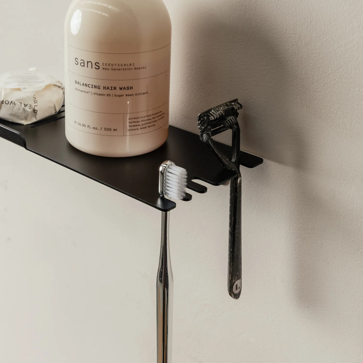 Close view of the black FOLD shower shelf with a pump bottle and razor